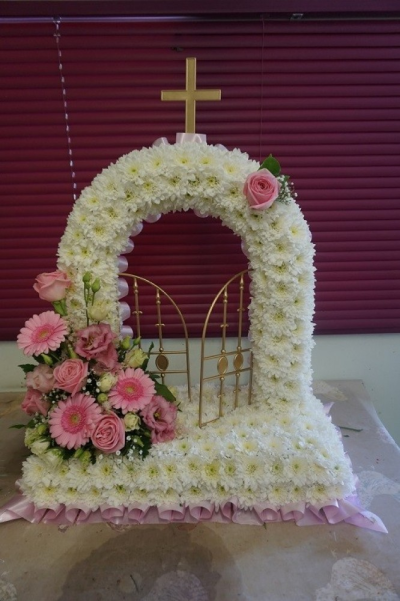 Gates of Heaven - At Sarah Coxon Floral Design we are delighted to present this product available for flower delivery in Mid and North Norfolk. 

This specialised tribute represents the Gates of Heaven and is based in white chrysanthemeums and edged in a colour co-ordinated ribbon. The spray on the side of the Gates includes a mixture of flowers such as Roses, Lisianthus, Spray Carnations and foliage,there is a single rose on the arch to complete the design. 

This is a freestanding design and can come in a variety of colours, please specify the colour of the ribbon and flowers you would like.

This stunning floral display has been arranged in water retaining foam (oasis) to ensure maximum freshness. 

We deliver directly to all of the local funeral directors and will contact them to confirm a delivery time. 

Our flowers at Sarah Coxon Floral Design arrive fresh from the Dutch auctions every day so you can be rest assured we are using the best quality of flowers available.